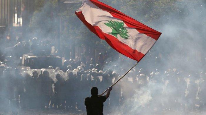 Seorang demonstran mengibarkan bendera Lebanon di depan pasukan polisi, dalam aksi unjuk rasa di Beirut, Lebanon, pada Sabtu (8/8/2020). Foto: Goran Tomasevic/Reuters. Seorang demonstran mengibarkan bendera Lebanon di depan pasukan polisi, dalam aksi unjuk rasa di Beirut, Lebanon, pada Sabtu (8/8/2020). Foto: Goran Tomasevic/Reuters.